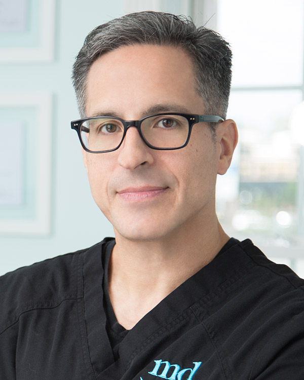 Headshot of Dr. Diaz wearing glasses and black scrubs with MD logo
