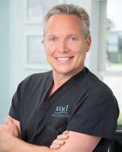 Dr. Christopher Thessen wearing black scrubs with the MD logo