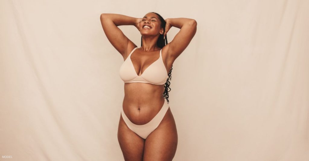 A woman in a beige bikini standing in front of a beige backdrop. (Model)
